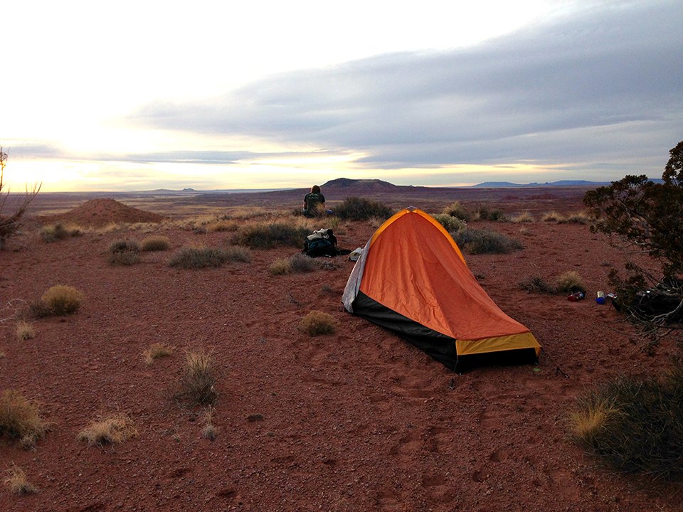 Small backpacking tent pitched on open desert ground in the Petrified Forest National Wilderness Area at sunset