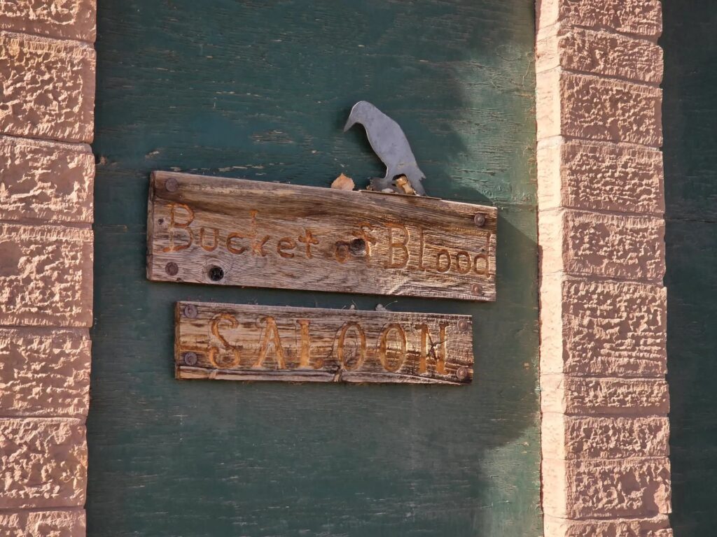 Weathered wooden Bucket of Blood and Saloon signs on a green board between sandstone pillars