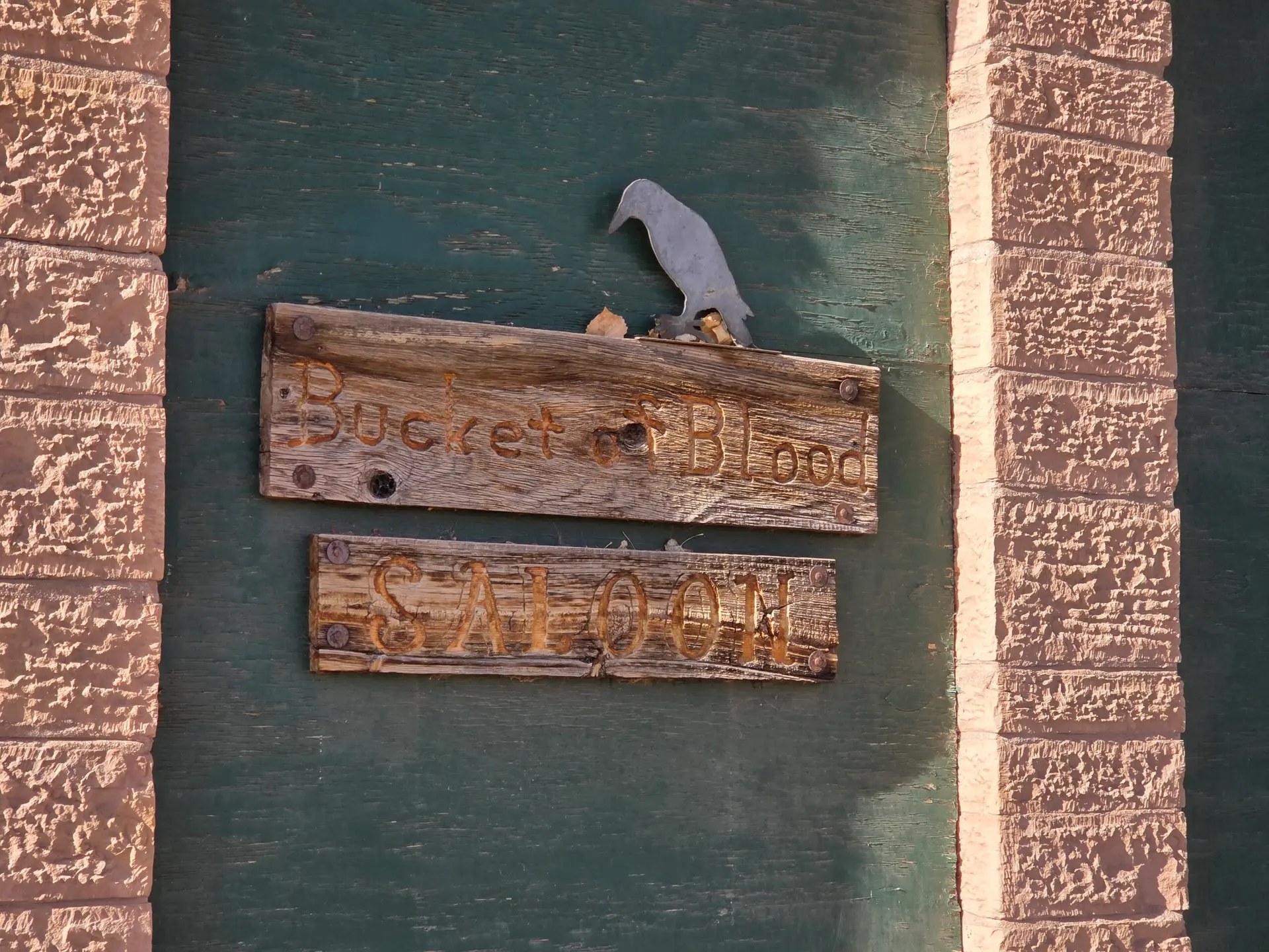 Weathered wooden Bucket of Blood and Saloon signs on a green board between sandstone pillars