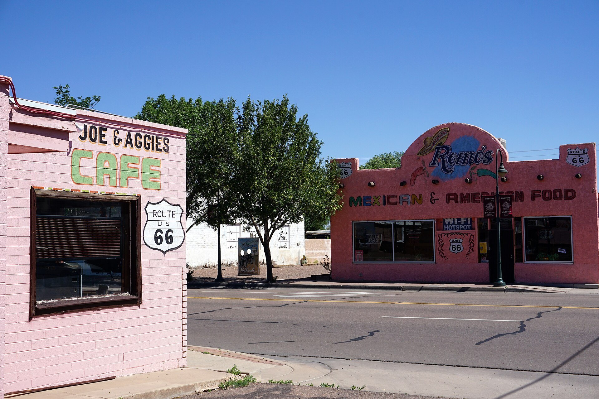 Pink adobe fronts of Romo's Mexican and American Food and Joe and Aggie's Cafe side by side on Hopi Drive in Holbrook, Arizona, under a blue sky