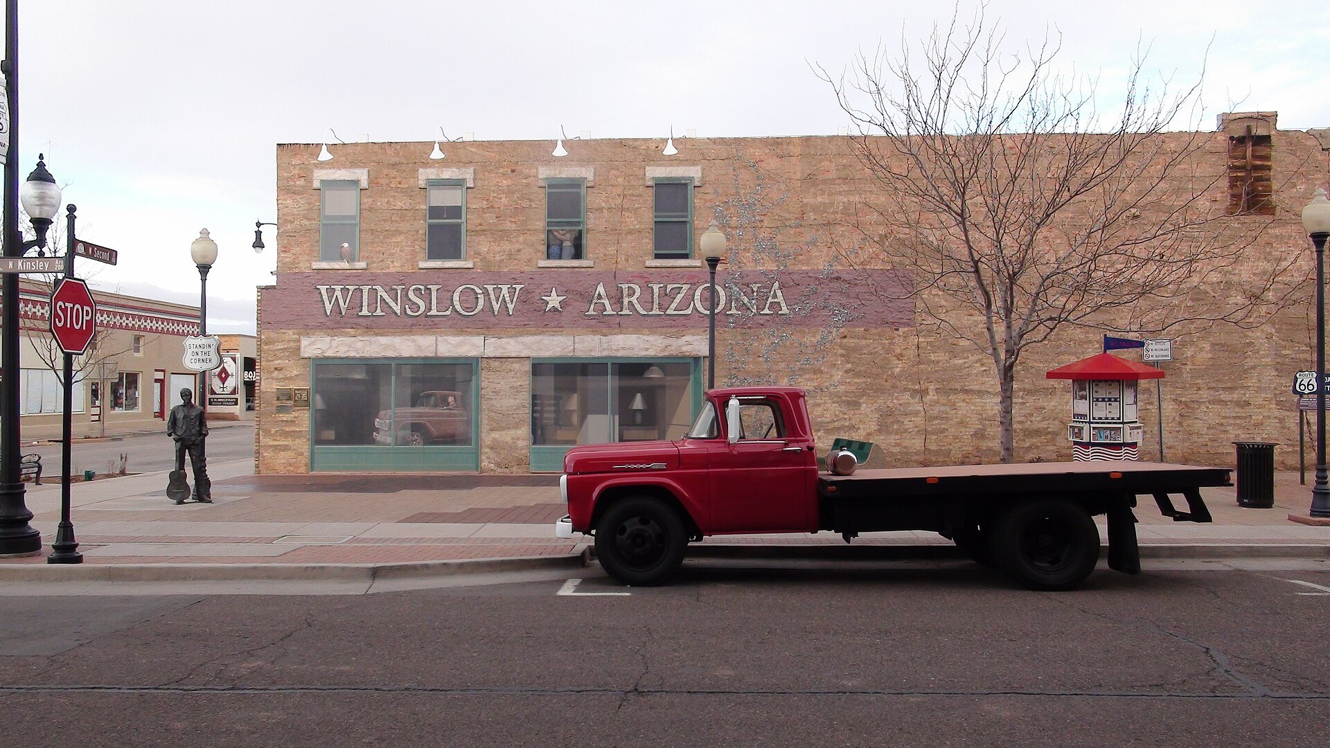 Red flatbed Ford parked in front of the mural at Standin' on the Corner Park in Winslow